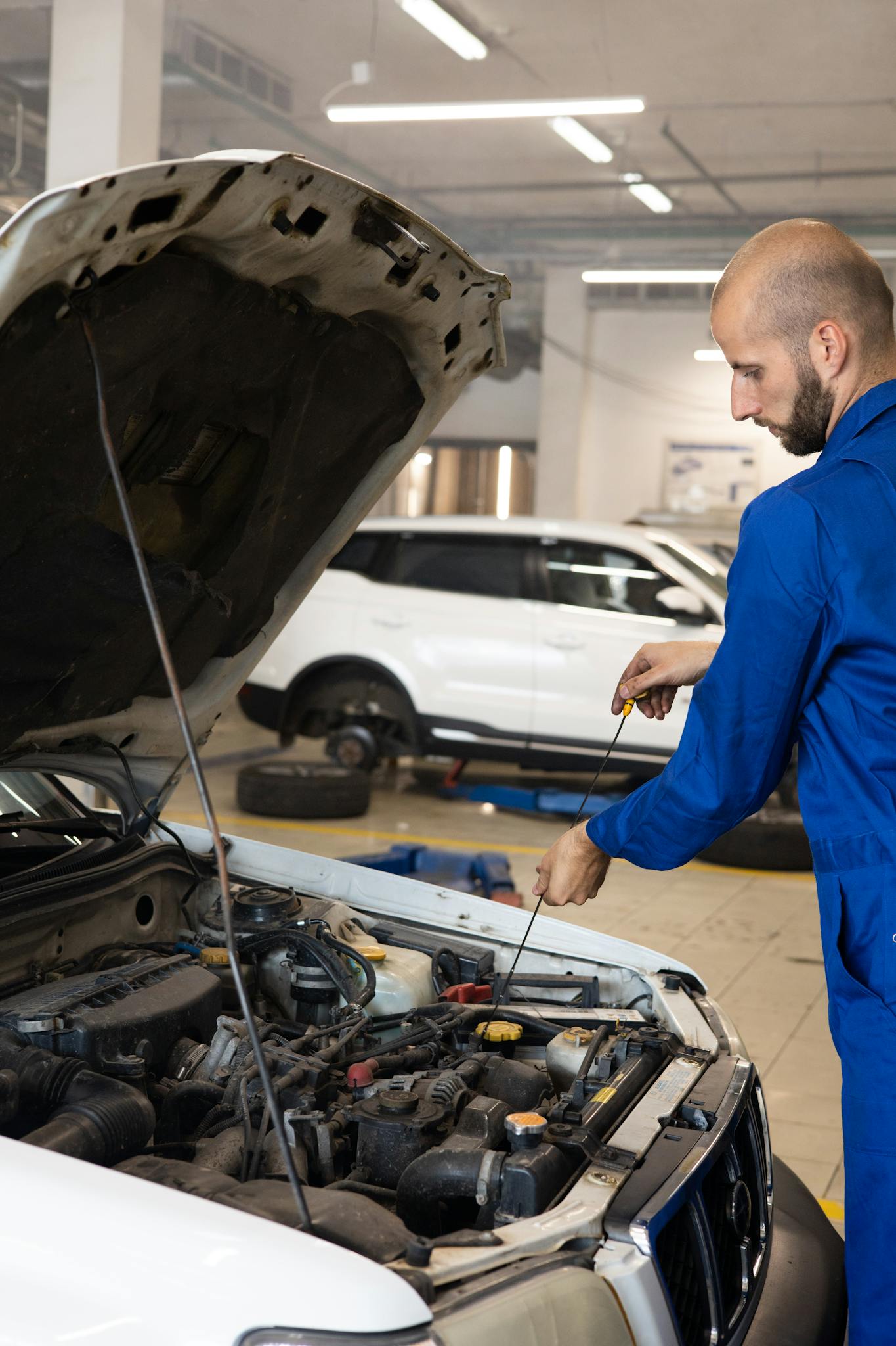 Auto mechanic in coveralls checking engine in repair shop. Vertical shot capturing maintenance process.
