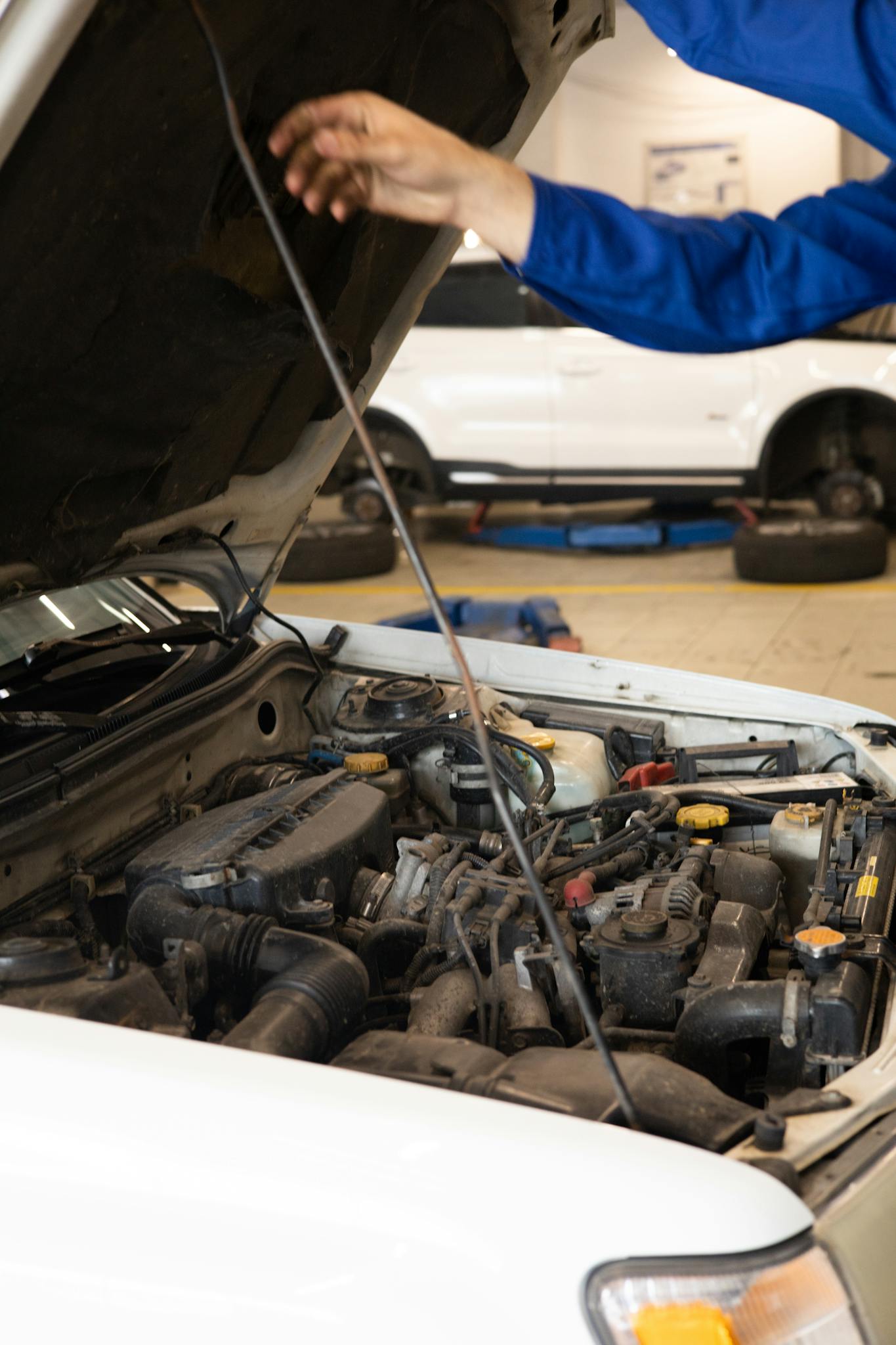 Close-up of mechanic inspecting car engine under open hood in an auto repair shop.